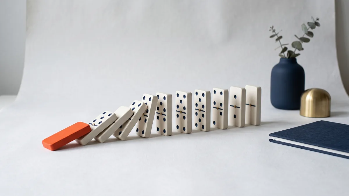 Row of dominoes toppling, started by one orange domino, the cover image for 5 SEO Mistakes Made by “Experts”