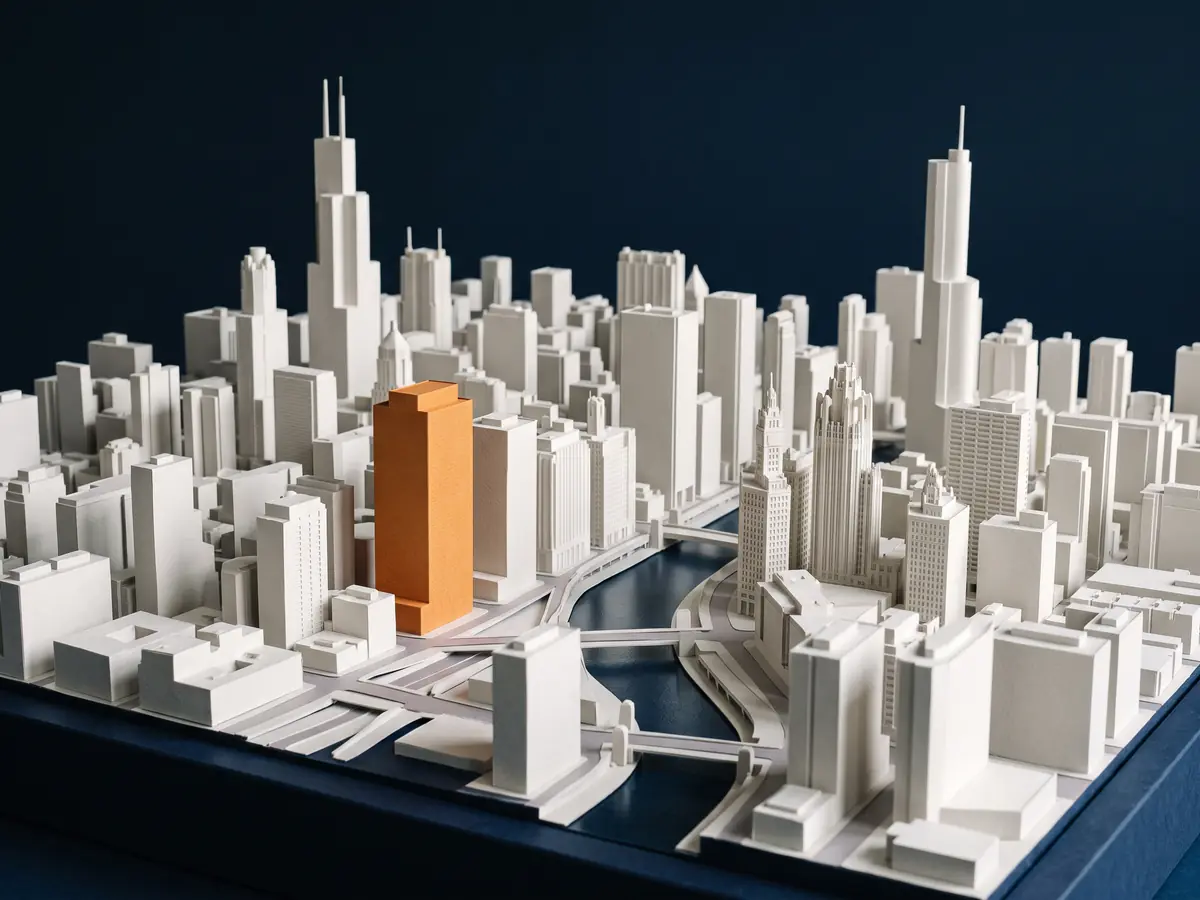 A paper model of downtown Chicago with one tower picked out in orange among white buildings